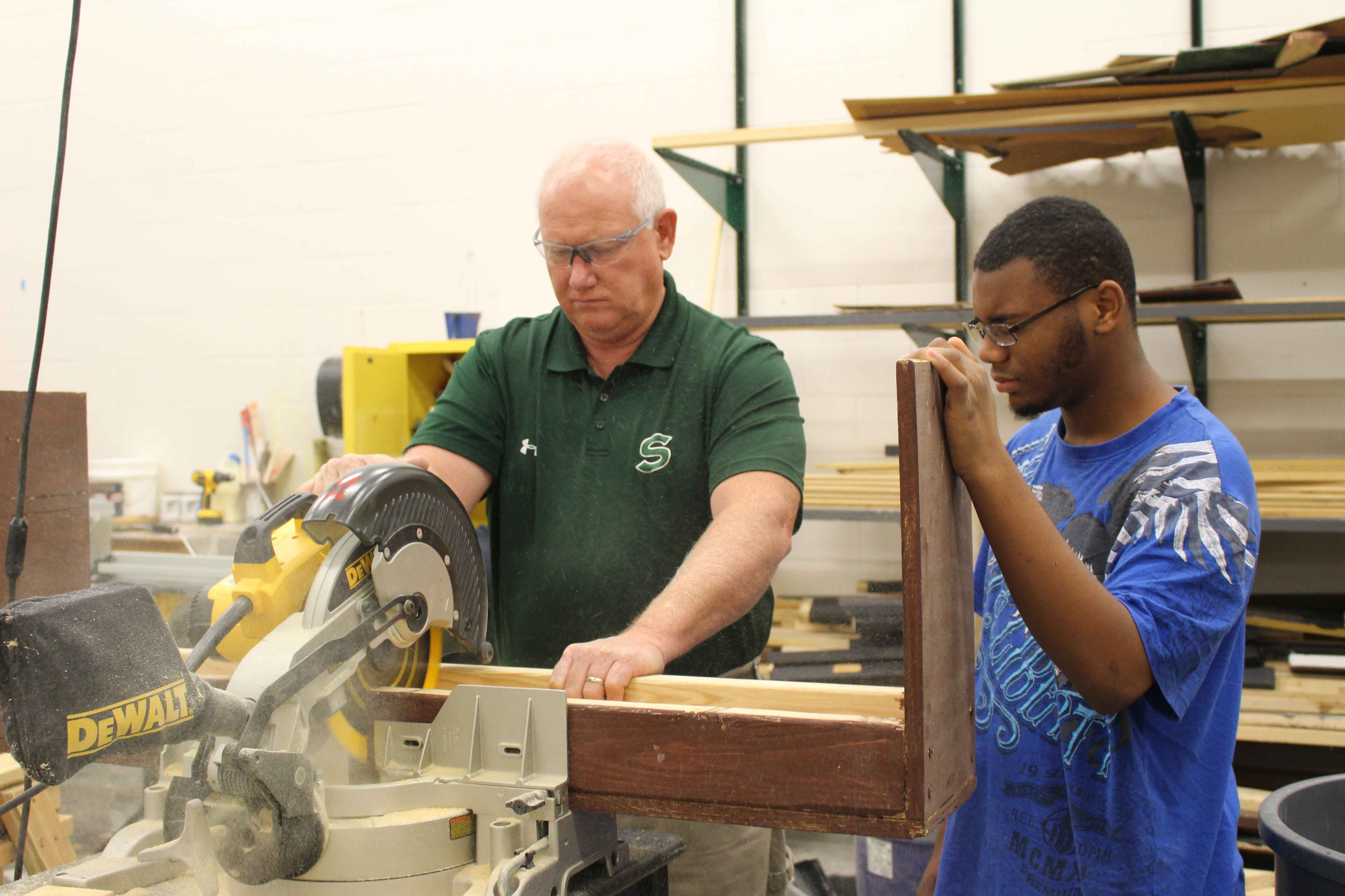 •Showing sophomore Jerry Burks how to cut a stool, teacher Stephen Dains prepares the props for the musical. The Stagecraft students have been working on the set a month in advanced. “We’re taking some of the old props that they had, and modifying them so that they work for what they’re doing this time,” said Dains. “We’re also building a few props from scratch.”